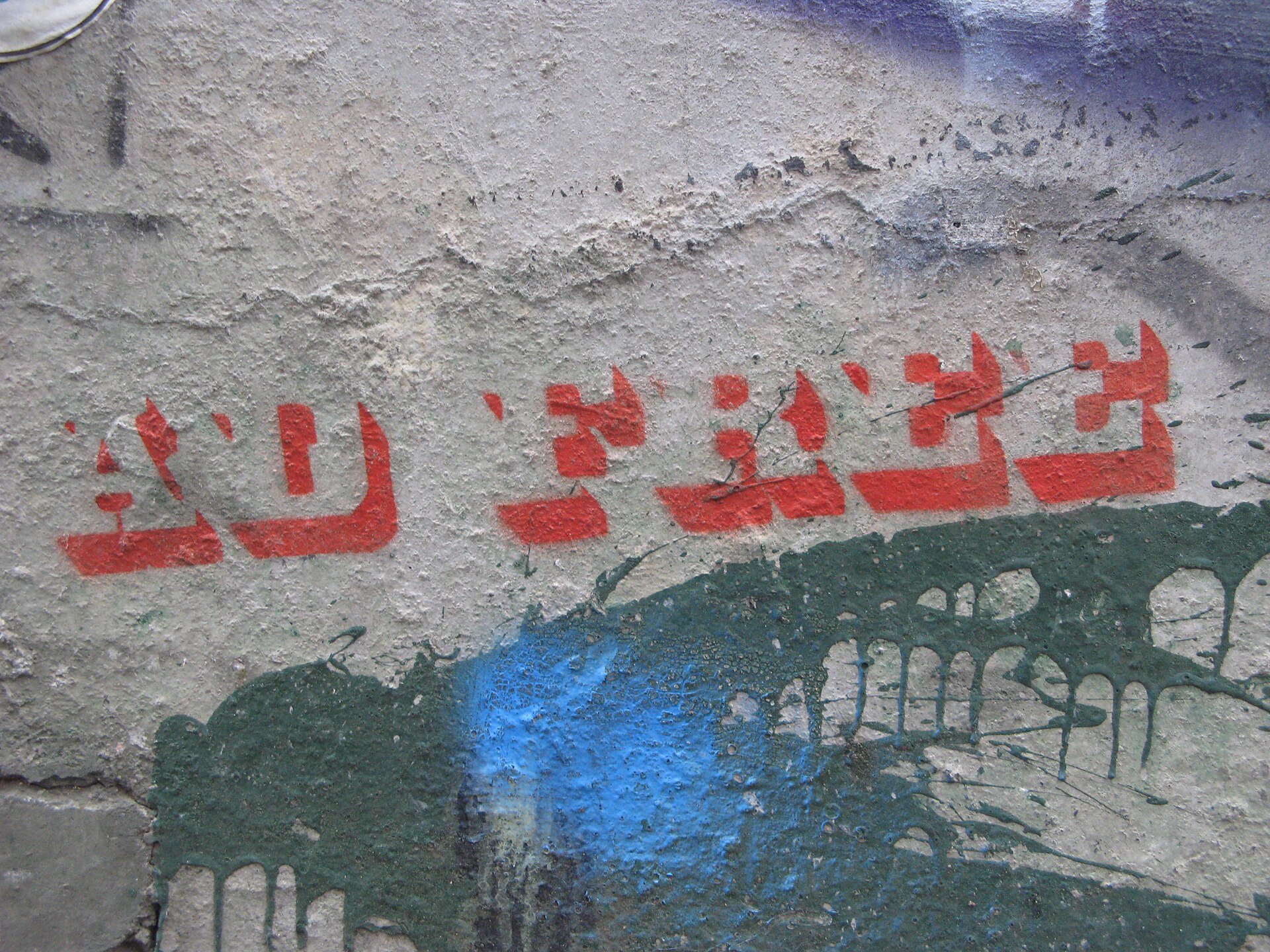 Red stencilled lettering on a cracked concrete wall under green and blue paint splatter